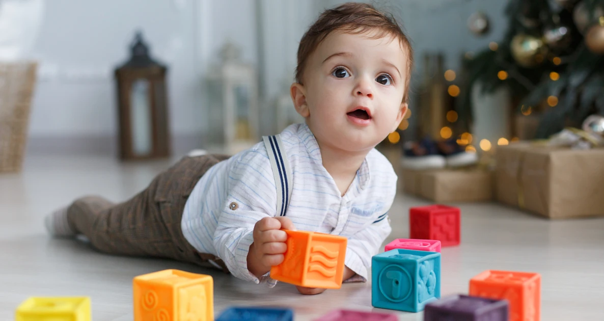 Baby plays with toy blocks in festive room with blurred lights.