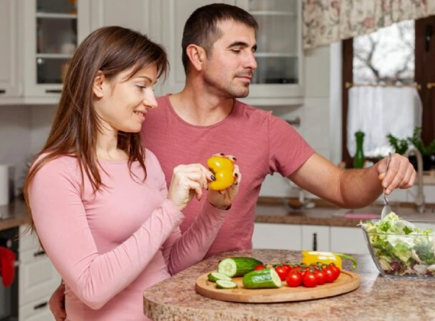 Couple smiles while chopping vegetables in the kitchen.