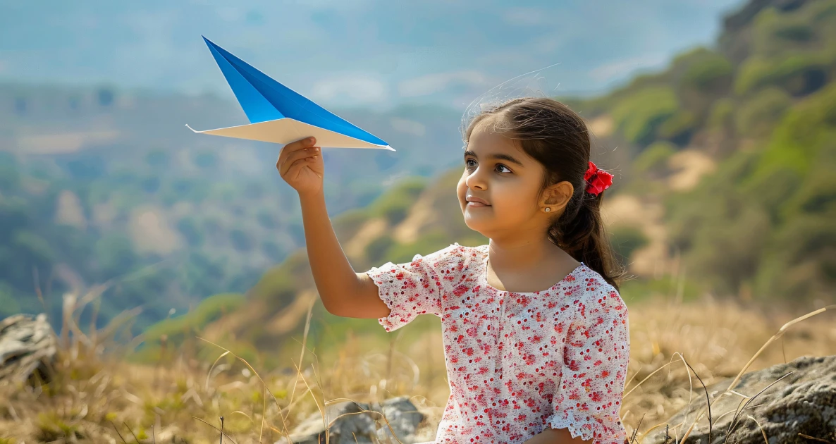Girl holding paper airplane in grassy field.