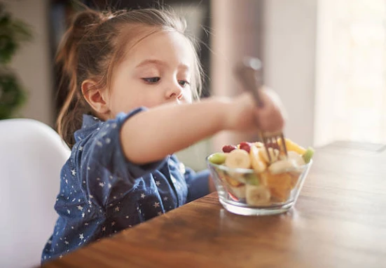 Girl reaches for fruit in a bowl, focused and curious.