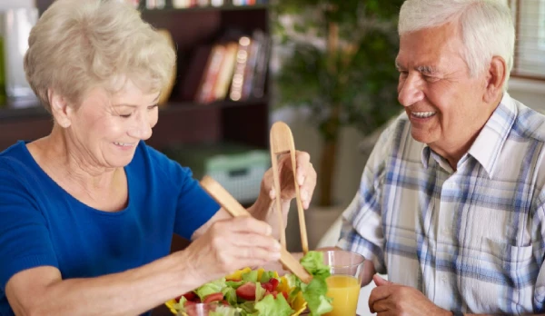 Elderly couple happily prepares a fresh salad.