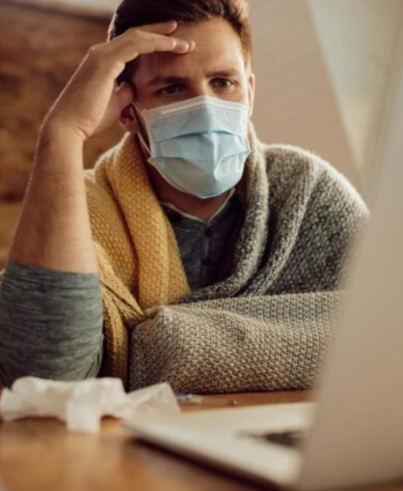 Man in mask with tissues using laptop while unwell