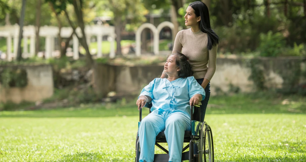 Young woman with a smiling elderly woman in a wheelchair in a sunny park.