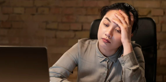 Tired woman rests head, looking at a laptop.