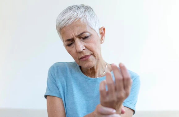 Elderly woman in blue shirt looks at her wrist in concern.
