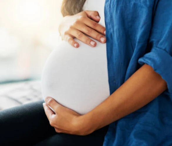 Pregnant person cradles belly in warm morning light.
