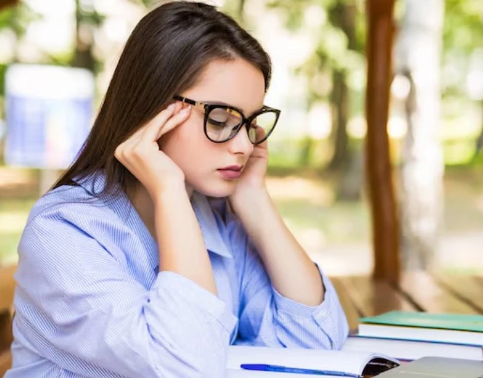 Woman with glasses studying outdoors, looking stressed.