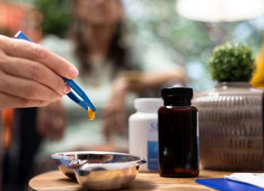 Hand holding capsule with tweezers over dish.