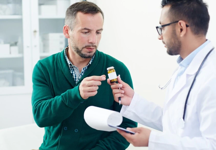 Doctor in white coat discussing medication with a man in a clinical setting.