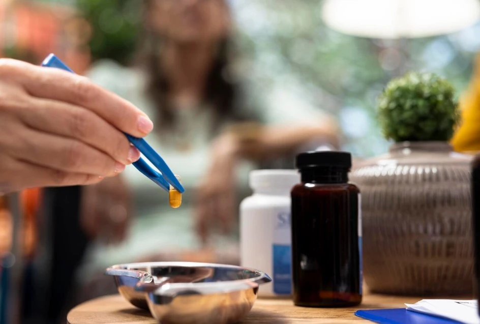 Tweezers holding capsule over bowl.