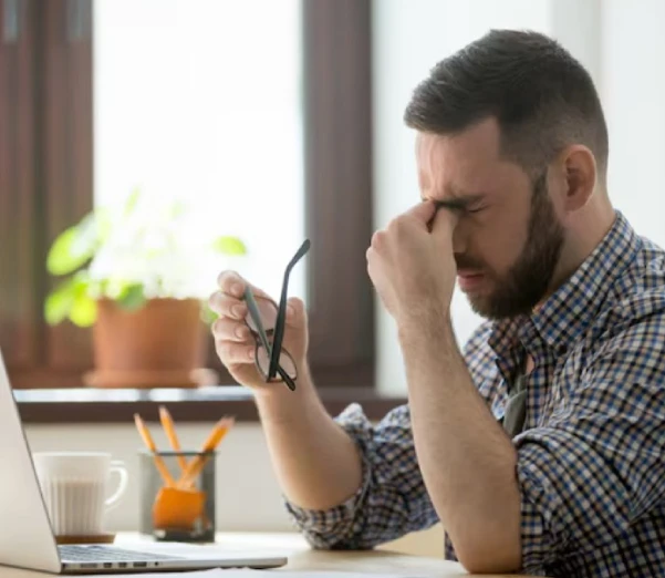 Man at desk rubbing eyes, looking fatigued.