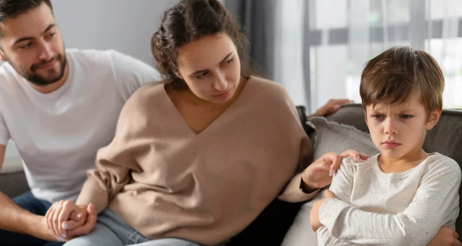 Couple comforting sad child on couch.