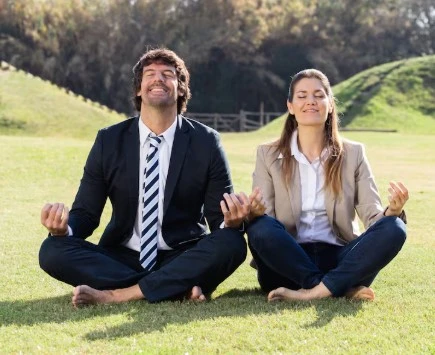 Man and woman meditate barefoot on grass, eyes closed.