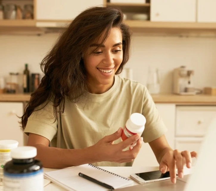 Woman holding supplement bottle, pointing at phone.