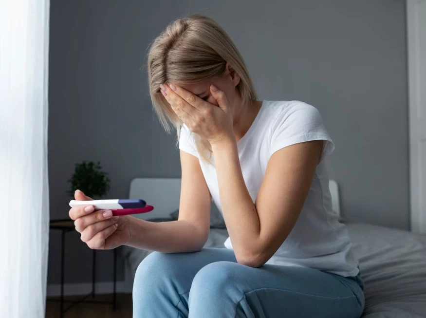 Woman on bed holding pregnancy test, emotional.