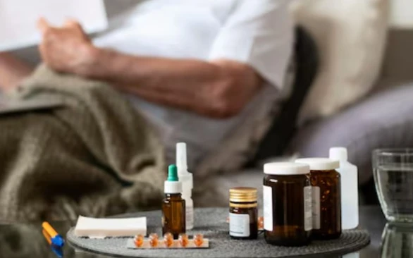 Sick person on sofa; medicines and water in focus, suggesting recovery.