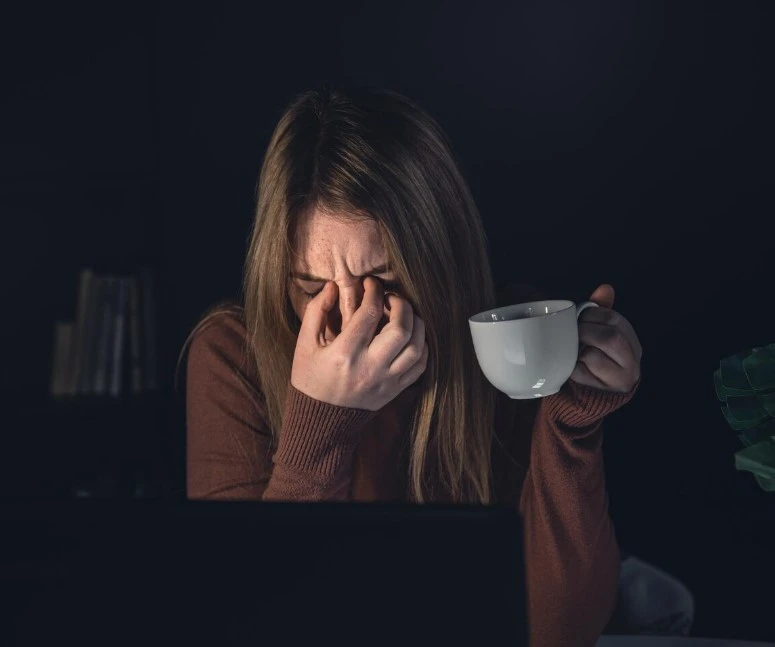 Stressed woman at laptop holding head, tired.