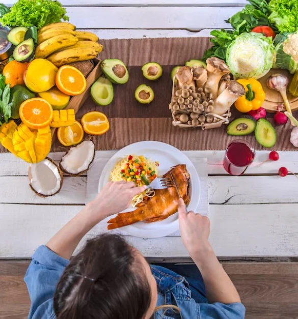 Woman cutting fish with pasta and vegetables, surrounded by fresh produce