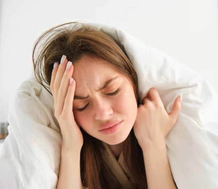 Woman in white blanket holding head with a pained, distressed expression.