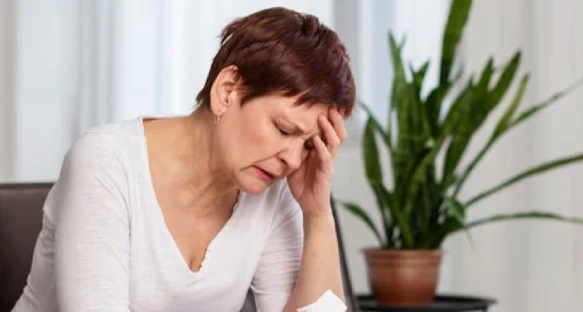 Woman in white shirt looking stressed, resting head.