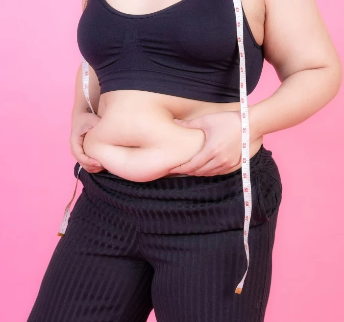 Person measuring waist with tape on pink background