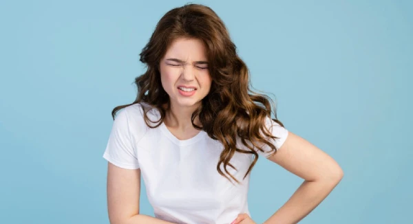 Woman in white shirt clutches stomach in pain.