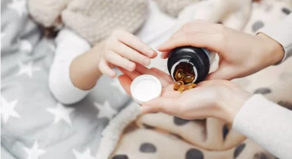 Child in bed takes vitamins from adult, cozy and caring.