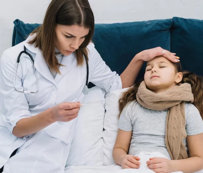 Doctor checks a sick girl’s temperature as she lies in bed.