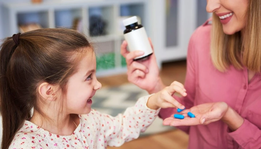 Woman gives blue pills to girl; warm, caring scene.