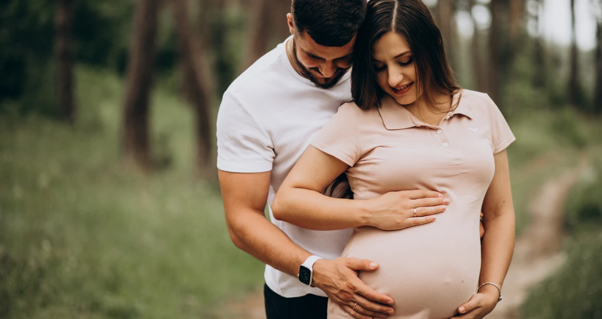Couple in forest, man embracing pregnant woman.