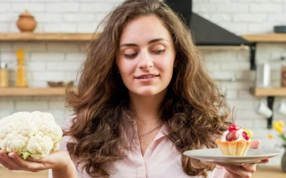 Woman choosing between cauliflower and fruit tart in kitchen