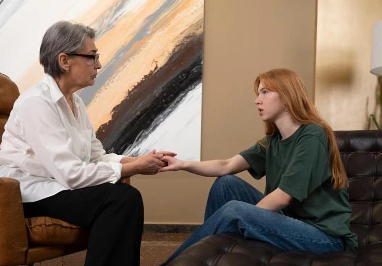 Two women hold hands in a counseling session.