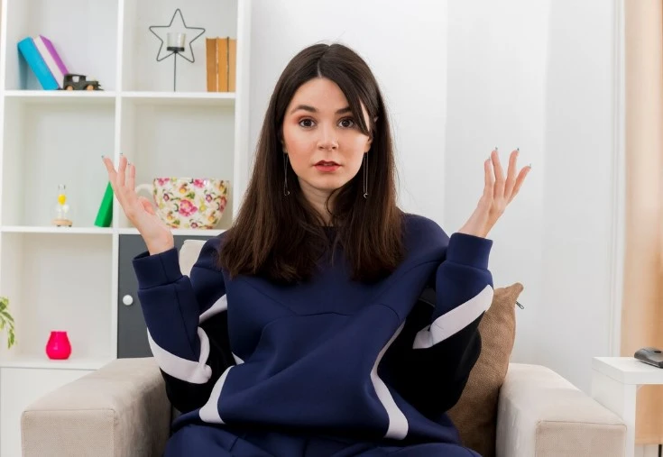 Confused woman sitting in chair with raised hands.