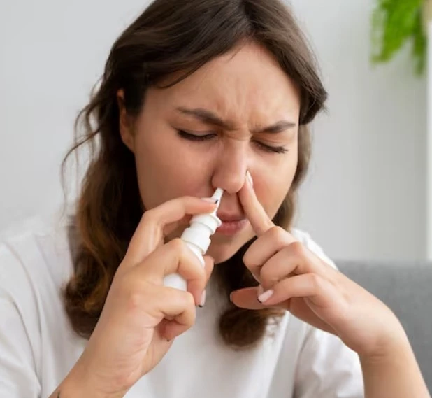 Woman using nasal spray, pinching nose.