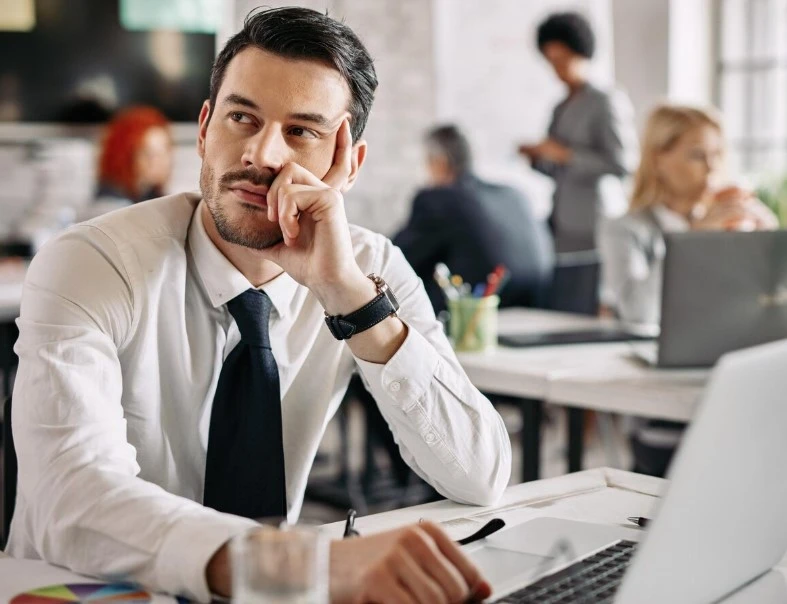 Man in office thinking with hand on chin.